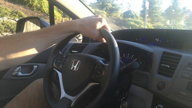 Why do men drive with one hand at the top of the steering wheel?
