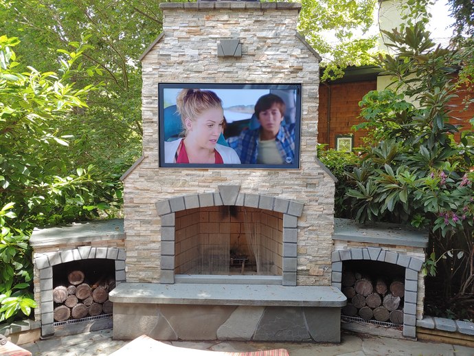 Outdoor 65" TV built into outdoor fireplace, rock speakers.