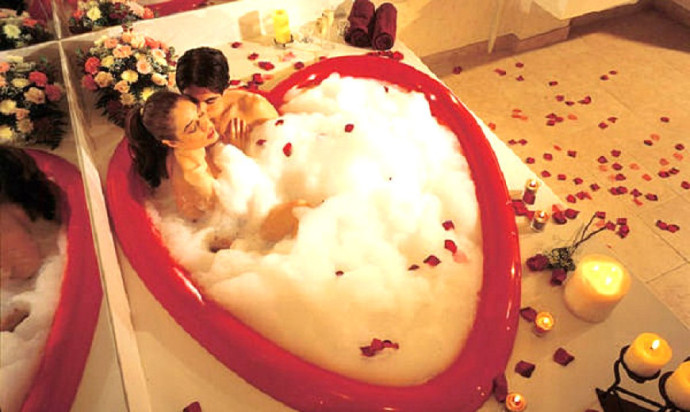 Couple enjoying a bubble bath in a heart-shaped bathtub.