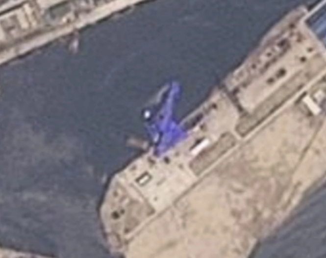 Grainy satellite photo of the ship, on its side, covered by a blue tarp