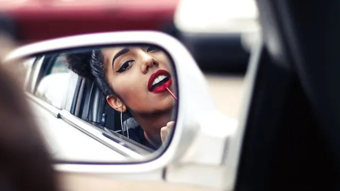 Why are women more than twice as likely to engage in risky behavior distracted driving by fixing their appearance while driving than men?